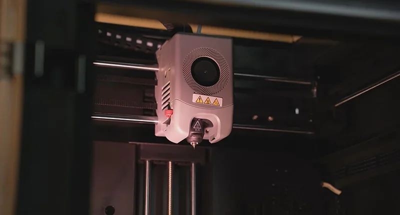 Flashforge Adventurer 5M Pro 3D printer nozzle inside the printing chamber, showcasing detailed mechanics and design in a dimly lit setting.