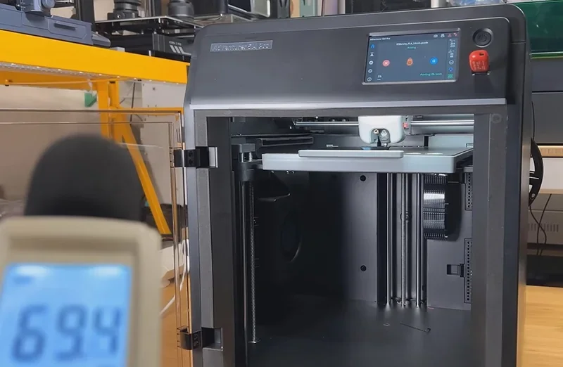 Flashforge Adventurer 5M Pro 3D printer with open chamber, digital display, and nearby decibel meter displaying 69.4, suggesting quiet operation.