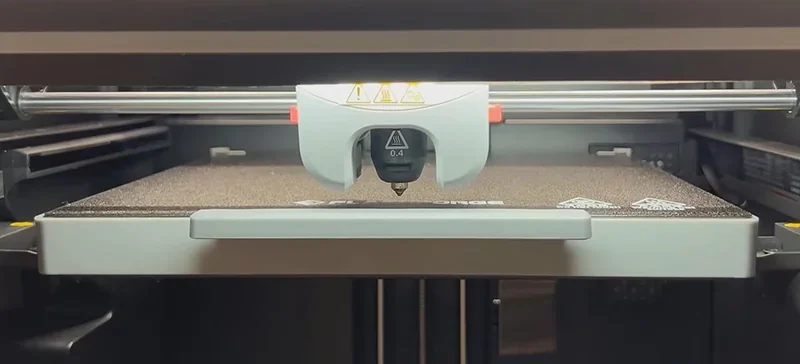 Flashforge Adventurer 5M Pro 3D printer close-up, showcasing extruder and build plate in a sleek, modern interior setting.