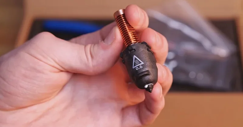 Hand holds Flashforge Adventurer 5M Pro's 0.6 nozzle with copper heatbreak, showcasing its detail and craftsmanship against a blurred background.