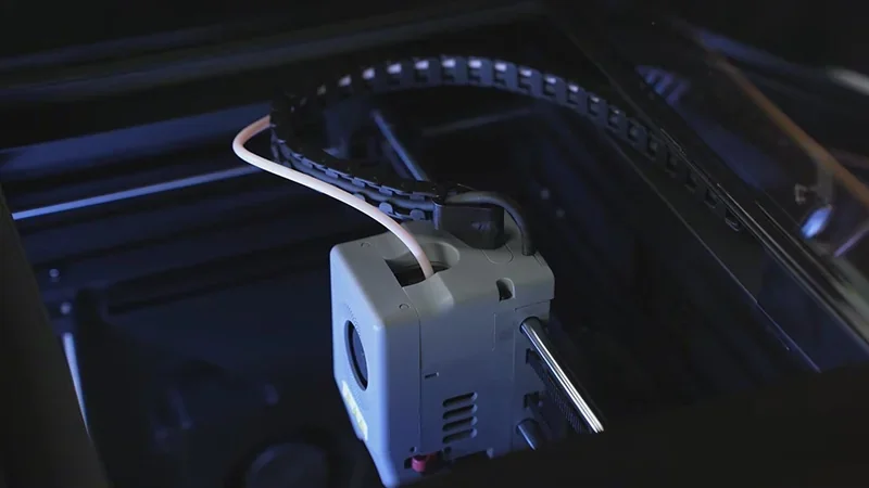 Flashforge Adventurer 5M Pro 3D printer interior showing filament feeding tube, extruder assembly, and print chamber with sleek black design.