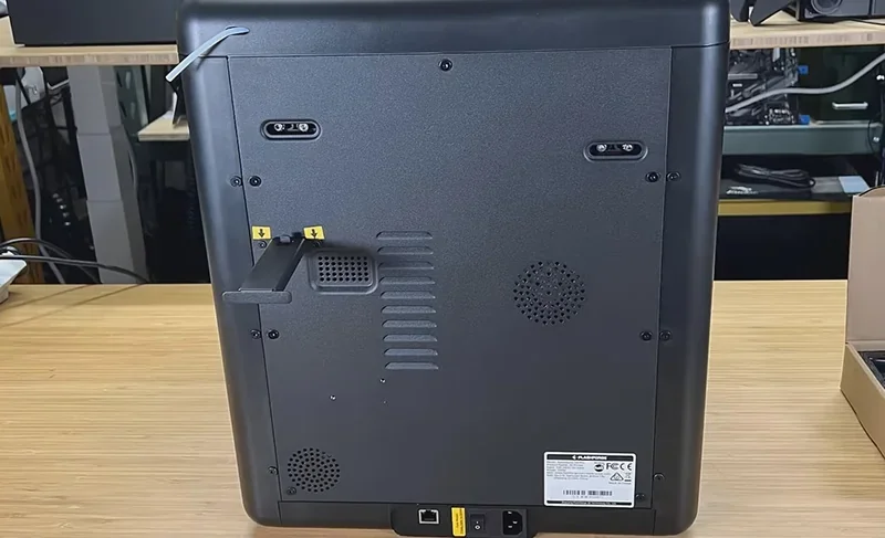 Flashforge Adventurer 5M Pro 3D printer showing back panel features, ventilation slots, and power connections on a wooden desk in a workshop setting.