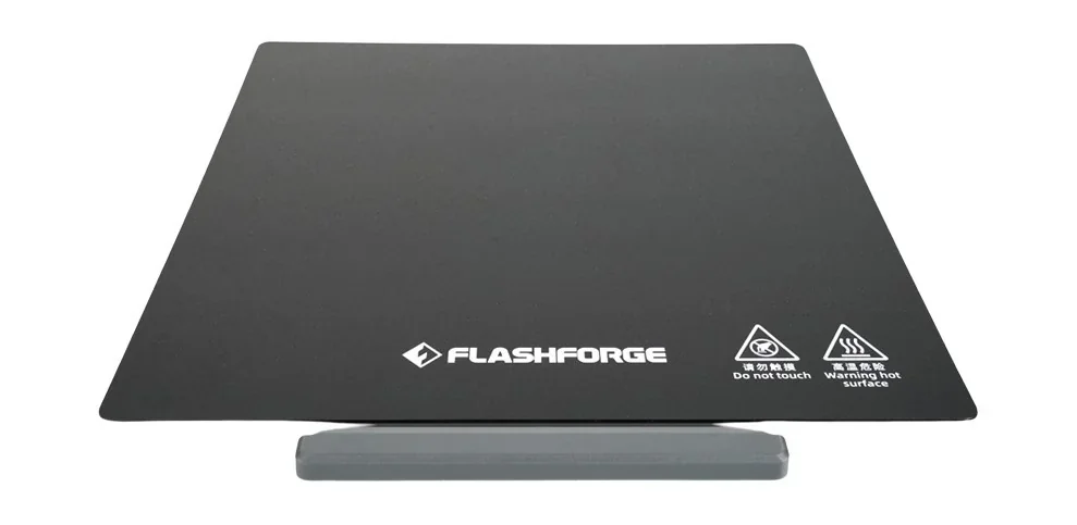 Flashforge Adventurer 5M Pro 3D printer heated bed with safety icons, branding, and warning text visible on a sleek black platform.
