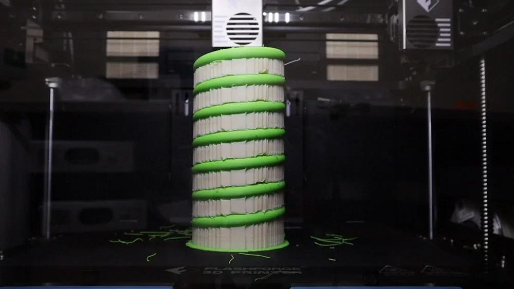 Flashforge Creator 4 printing a green and white cylindrical 3D model inside a transparent chamber.