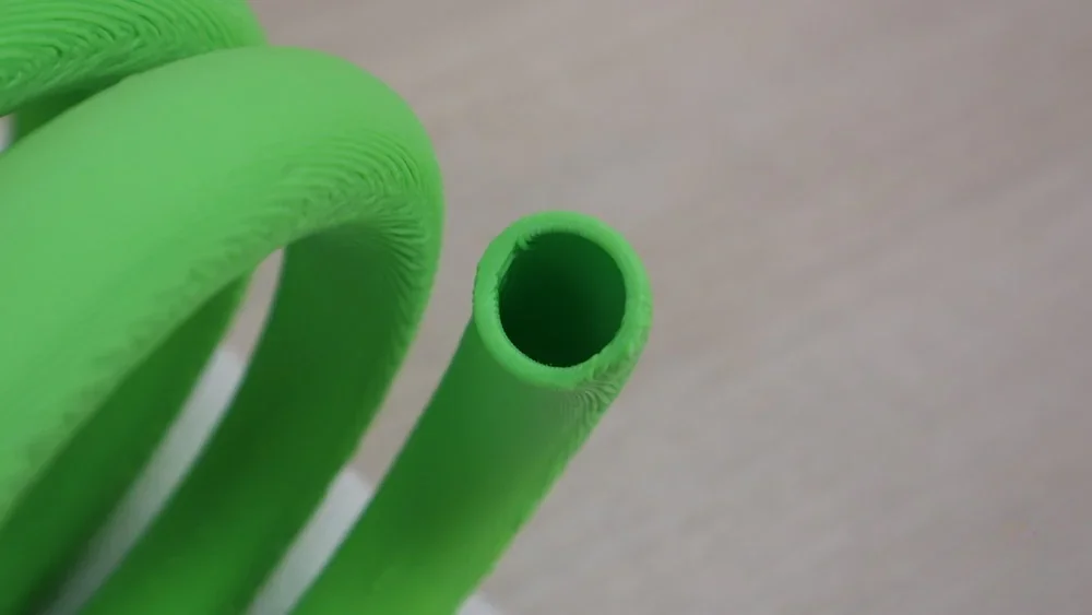 Green 3D-printed coil sample, likely made by the FlashForge Creator 4, showcasing precise detail and smooth texture on a neutral surface.
