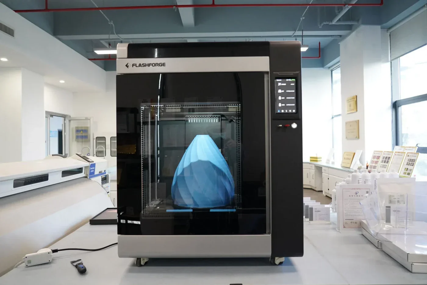 Flashforge Creator 4 3D printer in a lab setting with a large blue printed object inside, surrounded by lab equipment and branding visible.