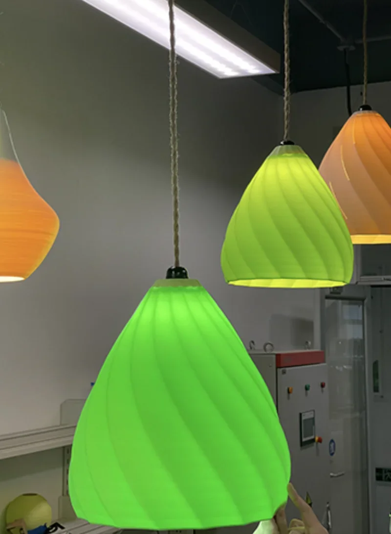 Colorful 3D-printed pendant lamps, green and orange, created by Flashforge Creator 4, hanging in a modern indoor setting.