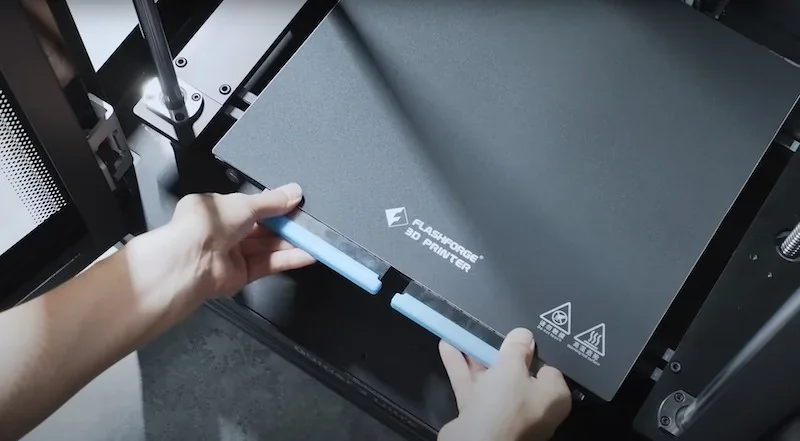 Flashforge Guider 3 Ultra 3D printer with branded tray being inserted by hands, showcasing operational setup and component design.