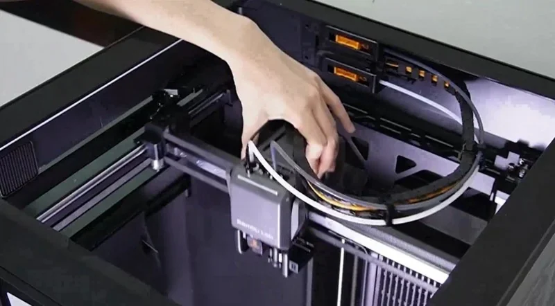 Hand inside h2c Bambu 3D printer adjusting part, showcasing interior mechanics with branding, highlighting high-precision design and functionality.