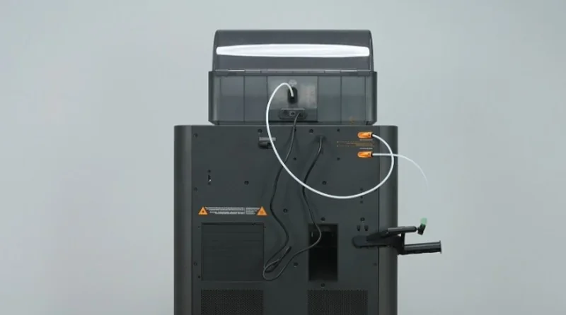 Black h2c Bambu 3D printer with filament connected at the back, showing wiring and ports.