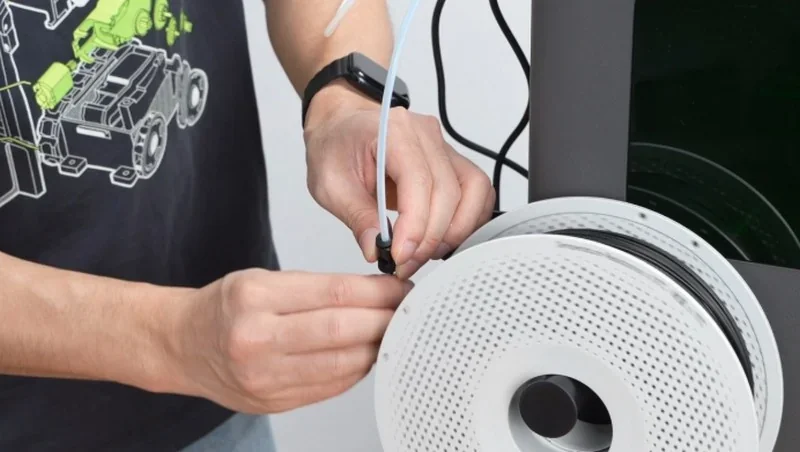Hands adjusting filament on h2c bambu 3D printer, showing spool, tubing, and part of the machine.