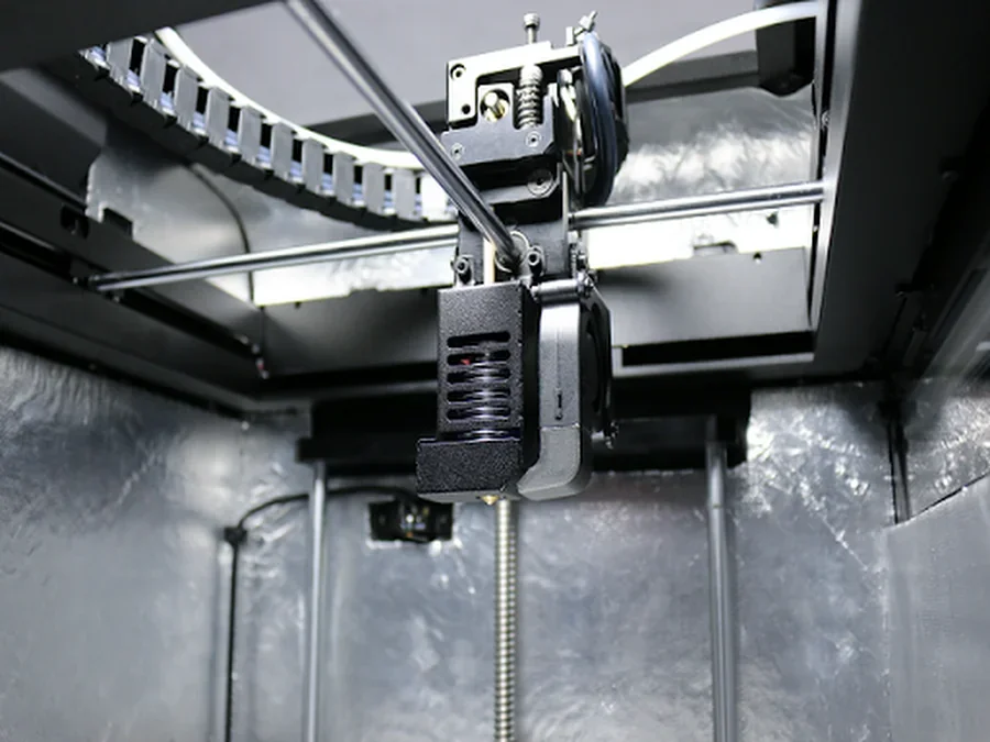 Intamsys Funmat HT 3D printer interior, showing mechanical components and extruder, surrounded by metallic and industrial setting.