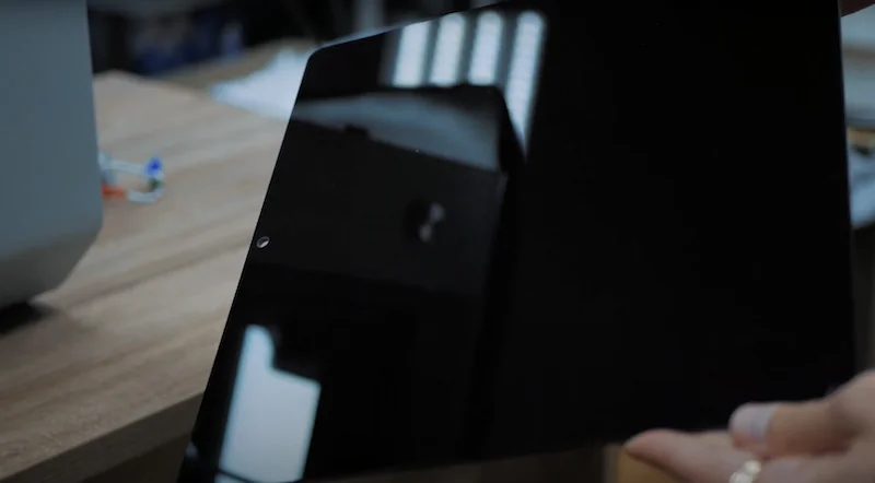 Black reflective panel held by hand on tabletop, likely from Intamsys Funmat HT 3D printer, reflecting overhead lights.