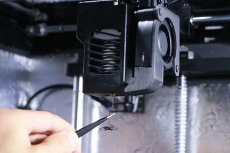 Close-up of intamsys funmat ht nozzle with hand using tweezers to remove filament.