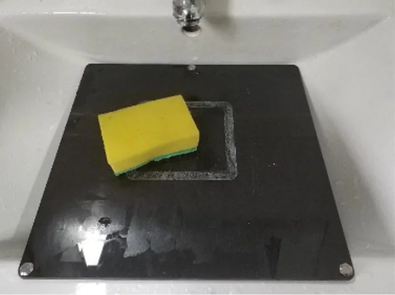 Yellow sponge on a black build plate, possibly cleaned, from an Intamsys Funmat HT 3D printer, in a sink setting.