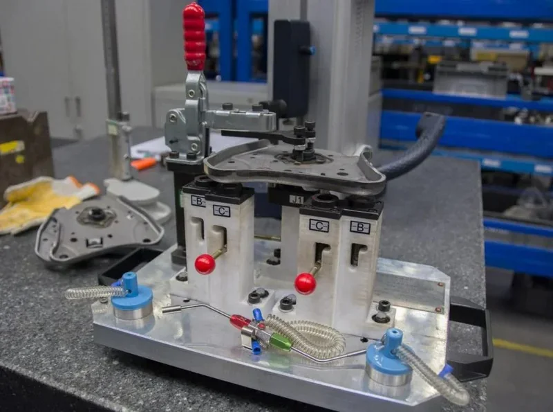 Intamsys Funmat HT 3D printed metal assembly fixture with clamps and levers on a workshop table, showcasing complex part creation.