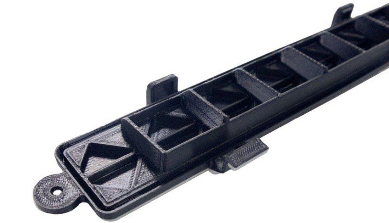 A 3D printed component created by the Intamsys Funmat Pro 310, showcasing a long, narrow, black object with geometric support structures. The component features a series of triangular and rectangular cutouts, highlighting the printer’s precision in creating intricate designs and details.