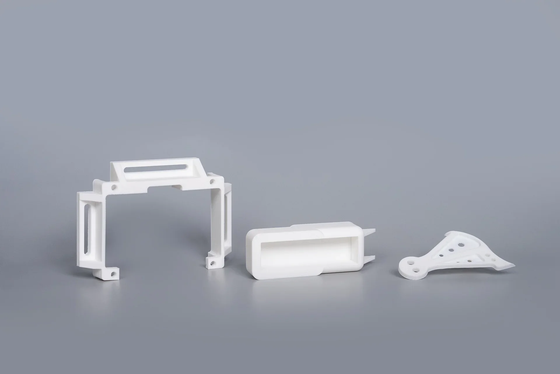 White 3D-printed parts from the intamsys funmat pro 310 on a gray background, featuring structural frames and geometric shapes.