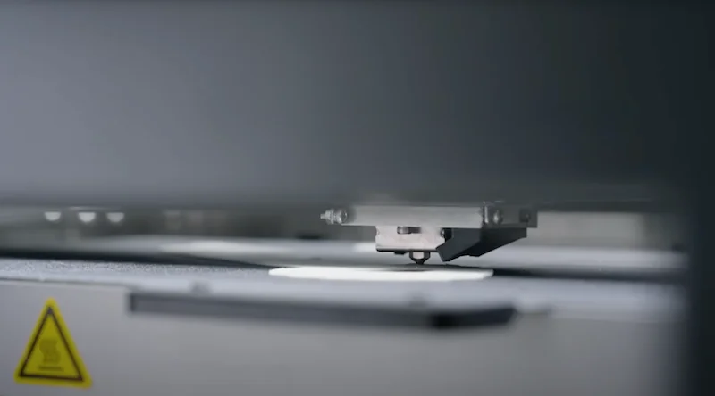 Intamsys Funmat Pro 310 3D printer in action, printing a white model on a flatbed, close-up view, industrial setting, caution label visible.