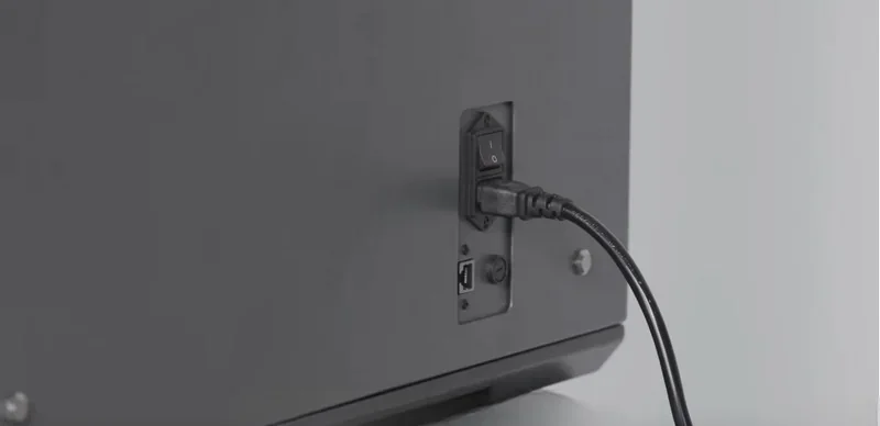 Intamsys Funmat Pro 310 back panel with a power switch and plugged-in cable, showcasing connectivity features against a grey background.