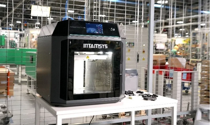 Intamsys Funmat Pro 310 3D printer in an industrial setting, placed on a table with printed parts nearby.