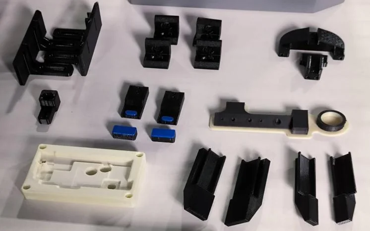3D-printed black and white parts arranged on the surface, created by the Intamsys Funmat Pro 310, showcasing precision and detail.