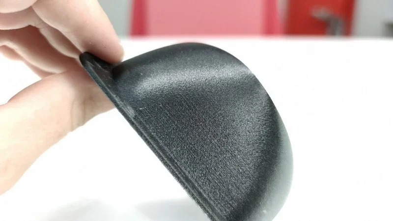 Black 3D printed component with a smooth finish, created by intamsys funmat pro 410, held against a red and white background.