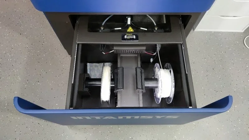 INTAMSYS Funmat Pro 410 3D printer's filament compartment with spools on a speckled floor, showcasing advanced dual extrusion capabilities.