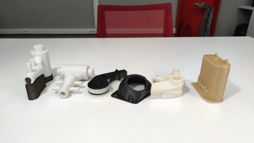 Samples produced by intamsys funmat pro 410 on a white table, showing various 3D-printed parts in different shapes and colors.