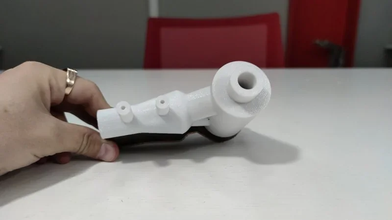 White 3D-printed part crafted by Intamsys Funmat Pro 410, held by a hand, on a white desk with a red chair and gray background.