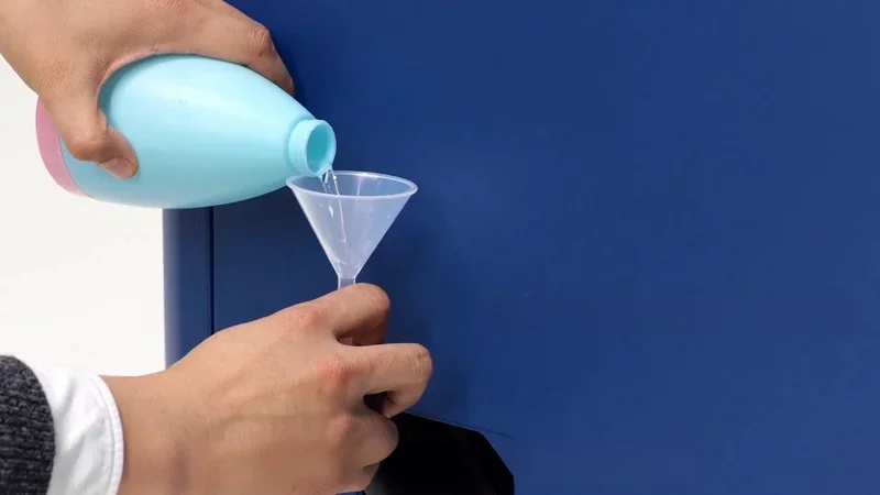 Pouring liquid into a funnel positioned at the Intamsys Funmat Pro 410 3D printer, emphasizing the machine's maintenance or setup process.