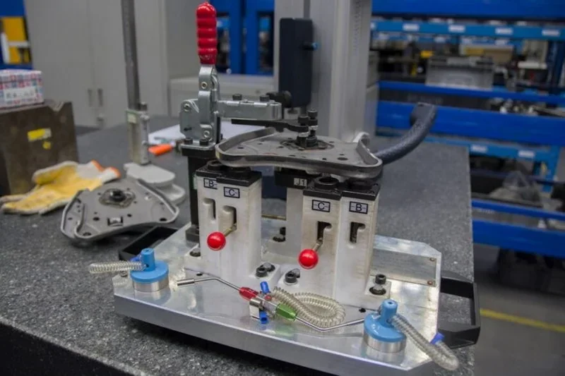 Jig assembly on workbench in industrial setting showcases parts created by Intamsys Funmat Pro 610 HT 3D printer, with visible machine components.