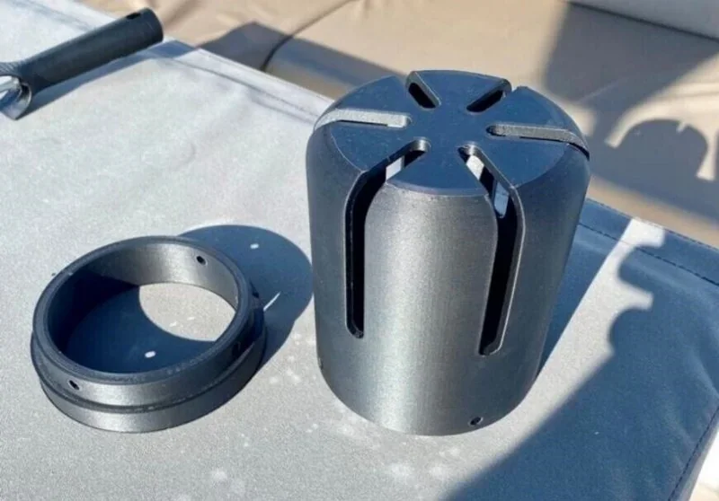 Two black cylindrical parts, featuring slits and smooth surfaces, created by the INTAMSYS FUNMAT PRO 610 HT 3D printer, displayed on a light surface.