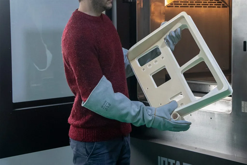 Person in gloves holds a 3D printed panel from the Intamsys Funmat Pro 610 HT, next to the printer, emphasizing its production capability.