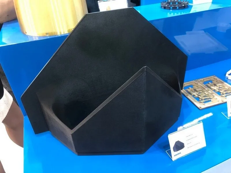 Black geometric 3D-printed part by Intamsys Funmat Pro 610 HT on display, set on a blue surface with branding visible.