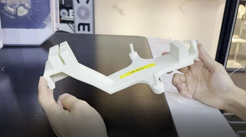 Hand holding 3D-printed white plastic part labeled 