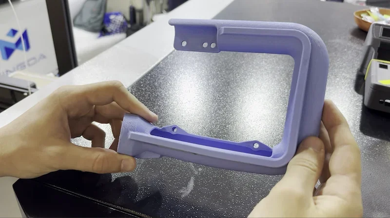 Hands hold a purple 3D-printed part created by the mingda md-400d on a textured black surface, with visible Mingda branding in the background.