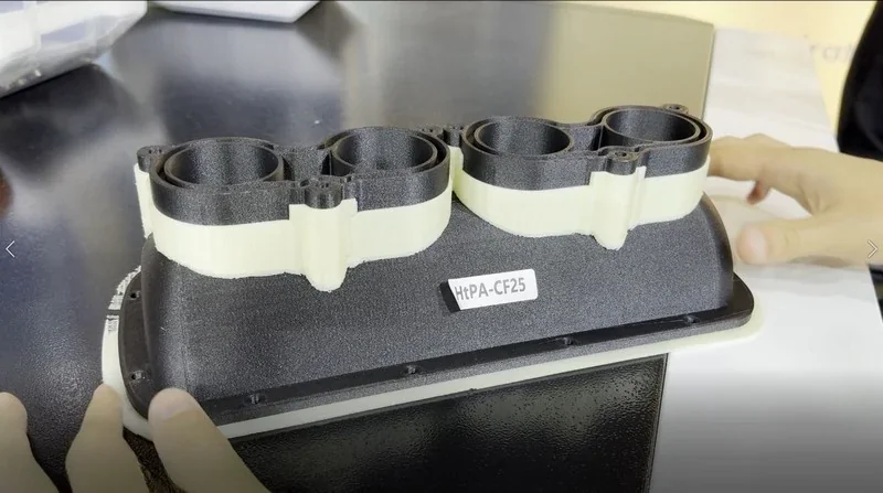 Mingda MD-400D 3D-printed black part labeled HPA-CF25 on a table, held by hands, showcasing precise multi-material printing.