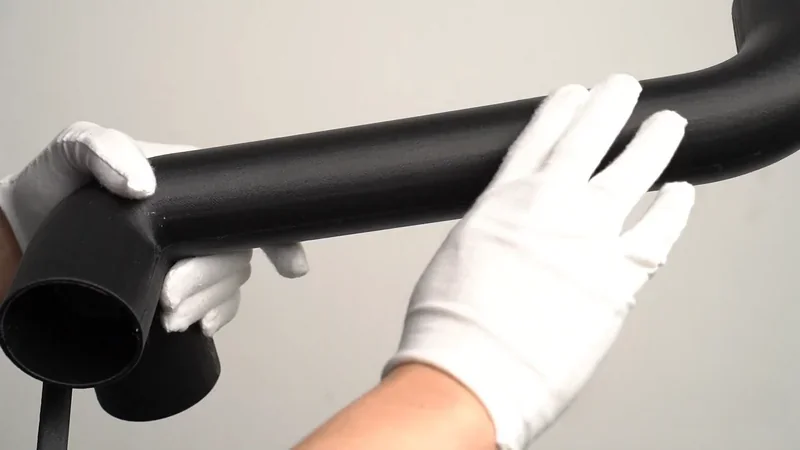 Gloved hands inspect a large, curved, black pipe 3D-printed using the mingda md-600d, highlighting the item's smooth finish and precise details.