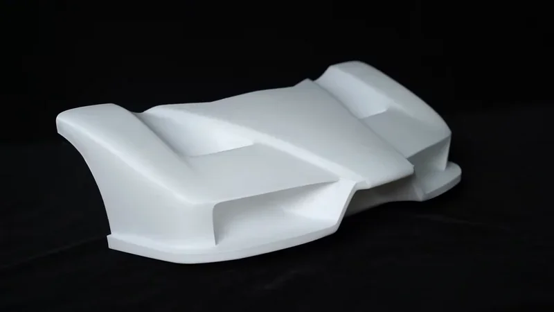 3D-printed aerodynamic car model in white, created by mingda md-600d, displayed on a dark background, highlighting its sleek, angular design.