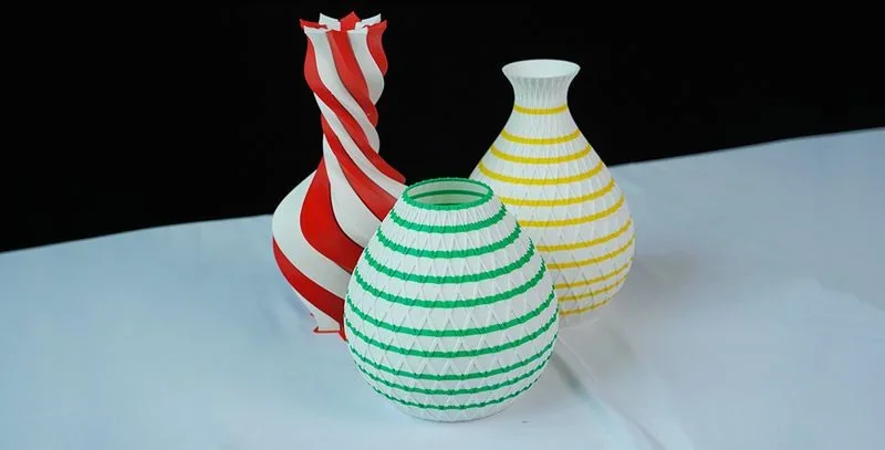 Three colorful 3D-printed vases with red, green, and yellow patterns created by the Mingda MD-600D, displayed on a white surface.