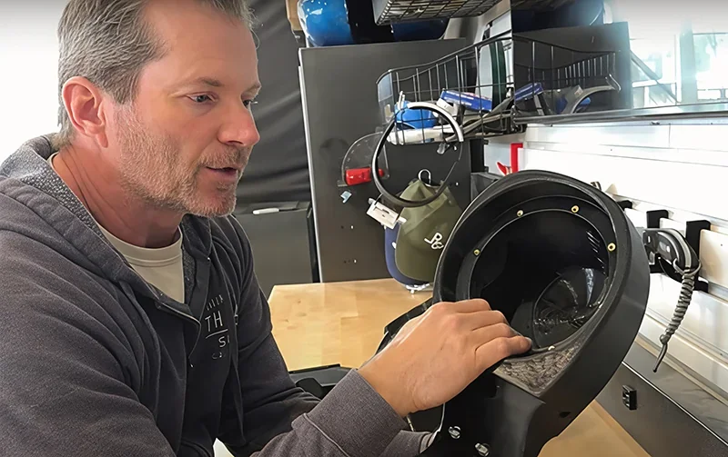Person examining a 3D-printed part created by Modix Big 120x in a workshop setting, surrounded by tools and equipment.