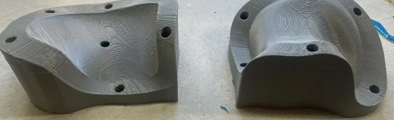 Modix Big 120x 3D-printed gray components with intricate contours and holes on a flat surface, showcasing advanced printing capabilities.