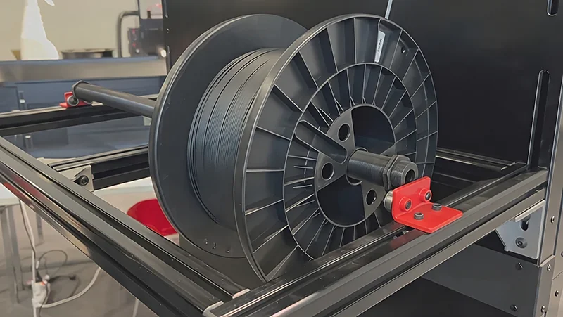 Modix Big 120Z 3D printer with large filament spool inside. Black and red components visible, showcasing industrial design and setup.