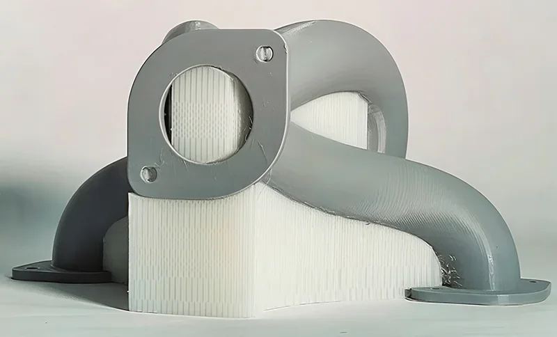Large 3D-printed gray and white curved duct piece created by Modix Big 120z, featuring detailed contours and mounting holes on a smooth flat surface.