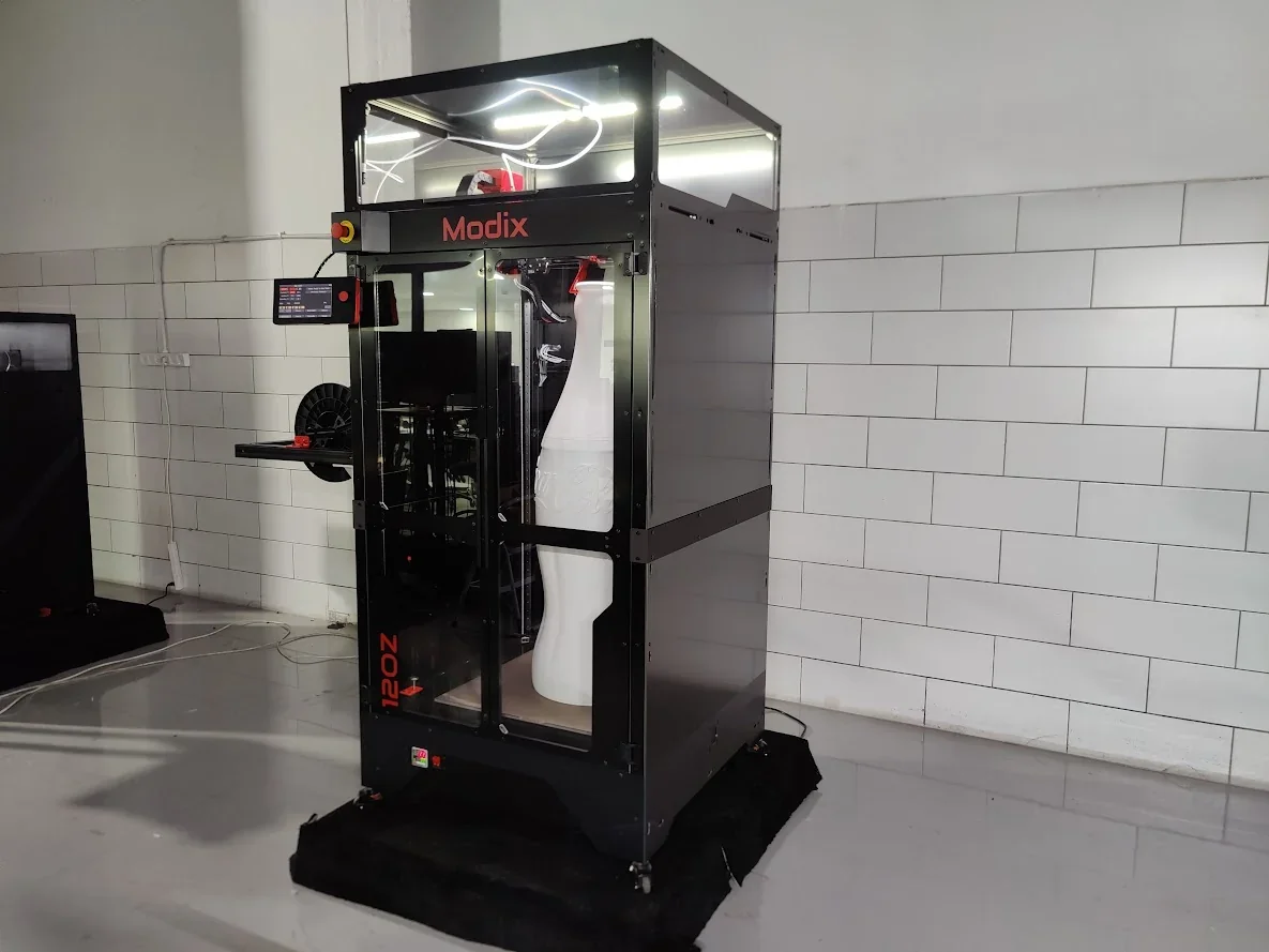 Modix Big 120Z 3D printer in a studio setting, featuring a large white part inside, visible branding, and control panel.