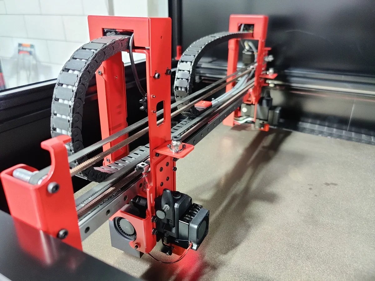 Modix Big 120Z 3D printer interior with red and black components, rail system, and cable management, showcasing precision engineering in an industrial setting.