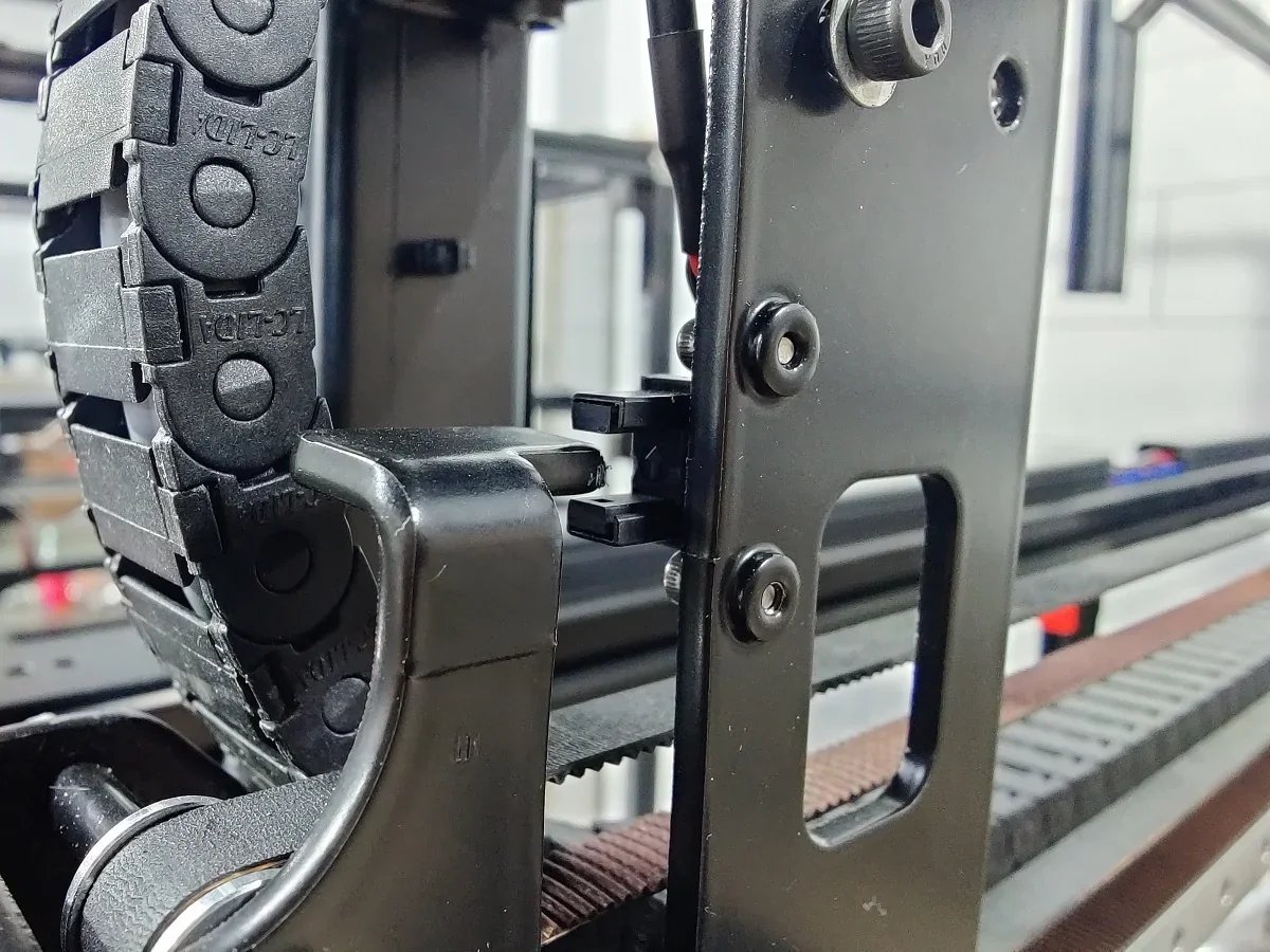 Modix Big 120Z 3D printer close-up showing detailed mechanisms, cable chains, and structural components in a workshop setting.