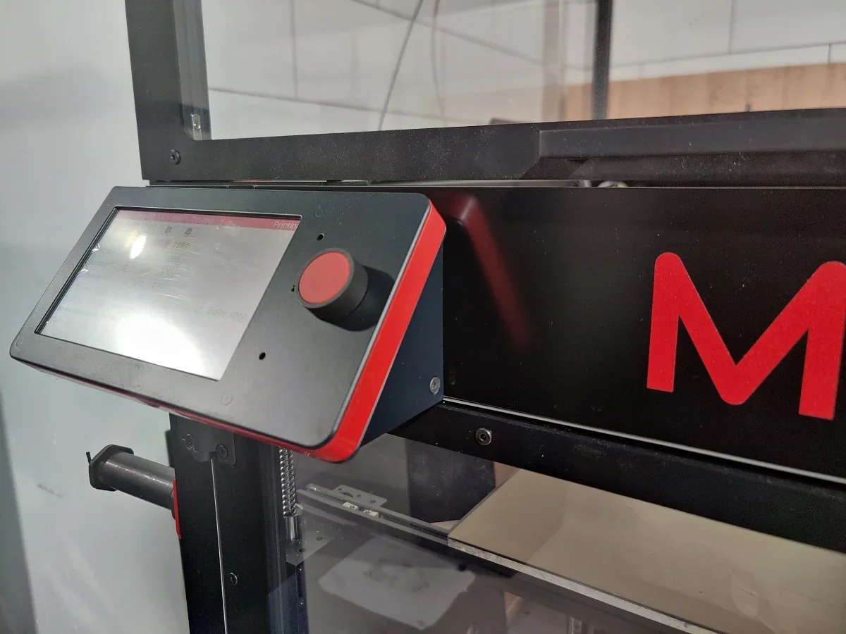 Modix Big 120Z 3D printer control panel with red knob and branding, surrounded by a clear enclosure in an industrial setting.