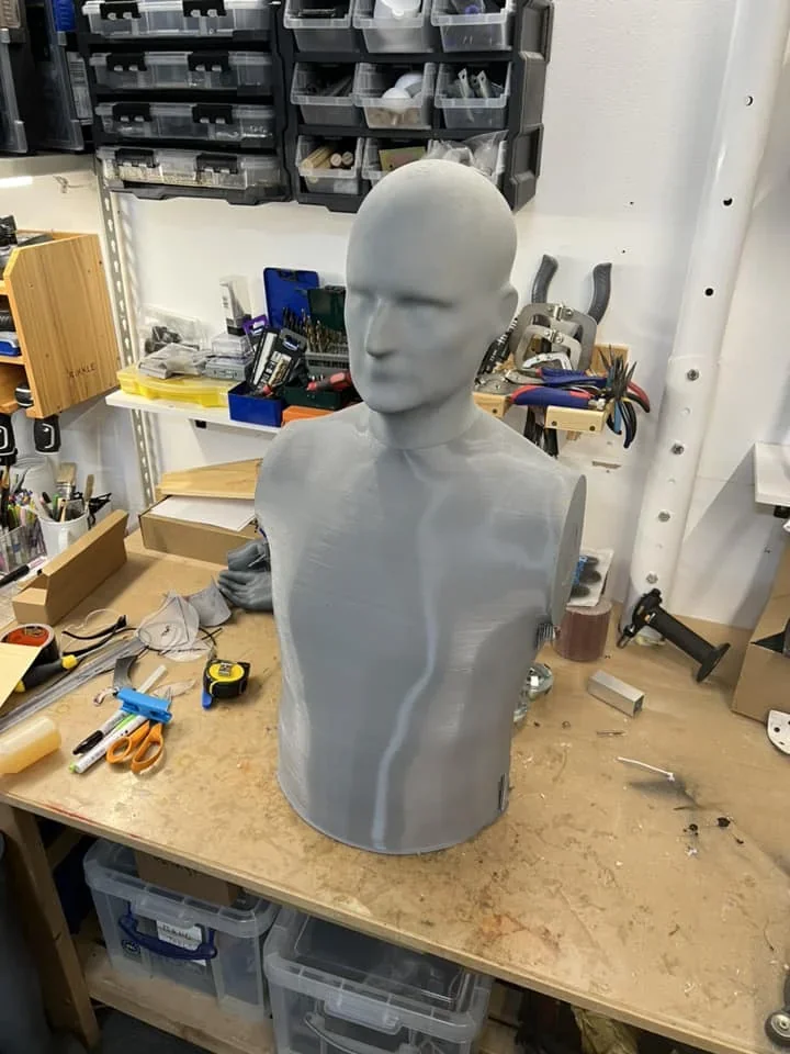 3D-printed gray bust on a workbench in a cluttered workshop, created by Modix Big 120Z 3D printer, surrounded by tools and storage bins.